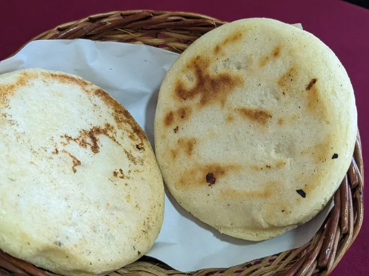 Two plain arepas in a basket, browned from the griddle